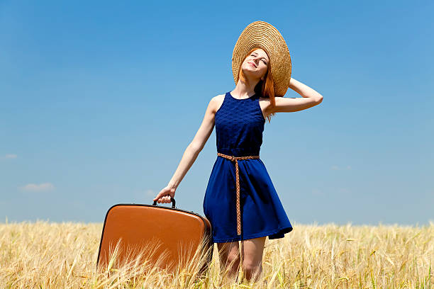 istock Redhead girl with suitcase at spring wheat field. 121906992