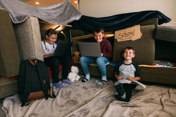 Children Homeschooling in a Couch Fort Young children are working on schooling and homework from laptops inside a home. They sit inside a homemade couch fort trying their best to replicate their elementary educations while at home during the coronavirus pandemic and social distancing guidelines. Image taken in Utah, USA. homeschooling photos stock pictures, royalty-free photos & images