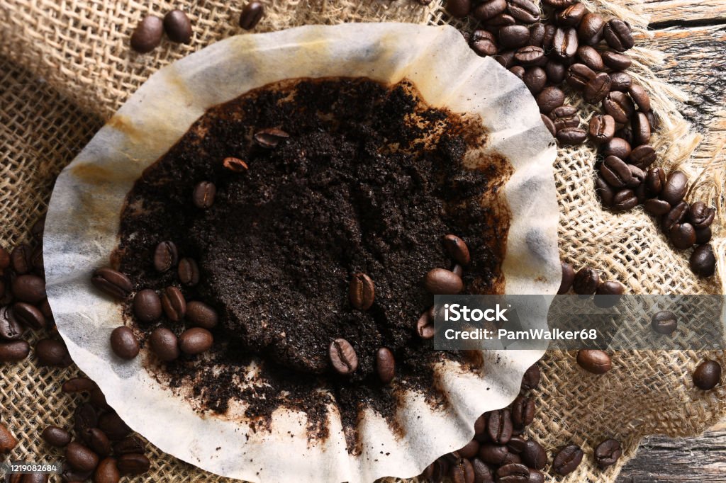 Old Used Coffee Filter An image of a used coffee filter with coffee beans and burlap cloth on an old wooden table. Ground Coffee Stock Photo