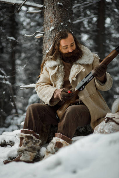 istock Brutal hunter in winter vintage clothes with beard loads ammunition in gun 1219095482