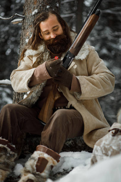 istock Brutal hunter in winter vintage clothes with beard loads ammunition in gun 1219096442
