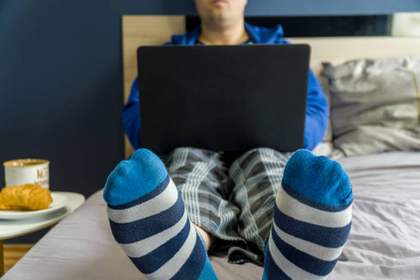 Home office concept - man working from his bed with breakfast stock photo