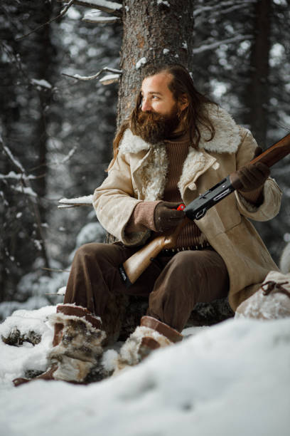 istock Brutal hunter in winter vintage clothes with beard loads ammunition in gun 1219100454