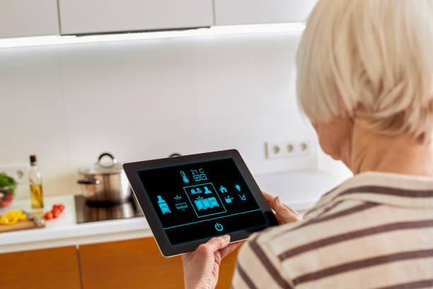 Retirement. Senior woman standing controlling smart home on digital tablet back view screen close-up