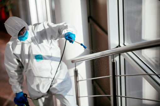 Man in protective suit disinfecting steps in building stock photo. Shadow DOF. Developed from RAW; retouched with special care and attention; Small amount of grain added for best final impression. 16 bit Adobe RGB color profile.