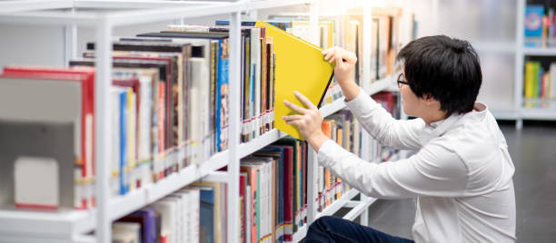 istock Asian man university student choosing book in library 1219109007