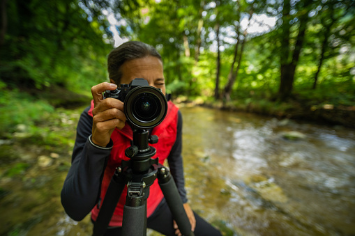 wideangle portrait shot of professional outdoor photographer female woman in river shallow depth of focus on camera with tripod