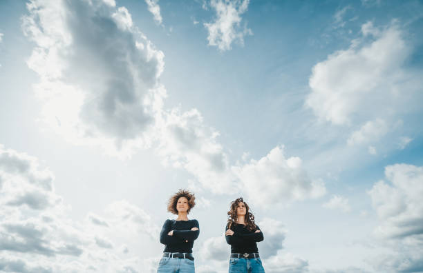 istock Two young woman in jeans posing against blue sky with clouds. Bottom view. 1219112551