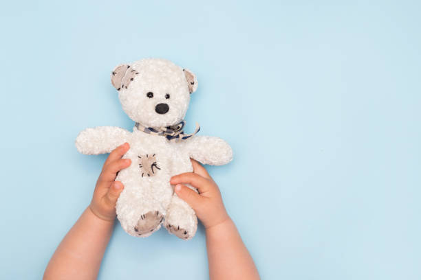 istock two kid hands hold a small toy teddy bear on a blue background, top view 1219120579