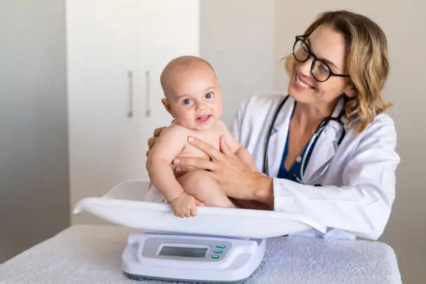 Photo of Smiling pediatrician weighing cute baby