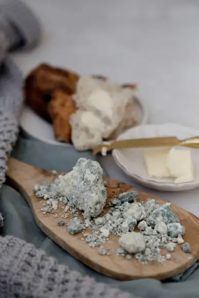 Vertical image of blue lamb cheese placed on a wooden olive board with negative space in upper right corner of the image.