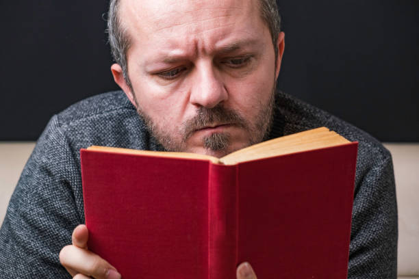 istock Bearded man reading red book on black background 1219123597