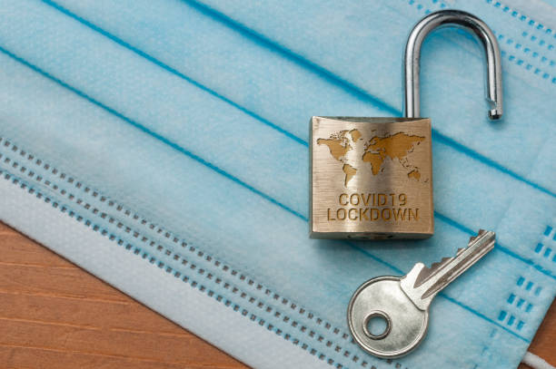 istock Coronavirus world lockdown end: an open lock with a world map and the word lockdown engraved and a key on a light blue surgical mask. 1219124013