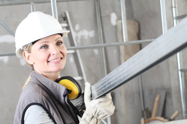 sonrisa mujer constructor a construir retrato con casco blanco y auriculares de protección auditiva, sosteniendo un perno de metal para paneles de yeso en el fondo del edificio del sitio interior con andamios - metal stud fotografías e imágenes de stock