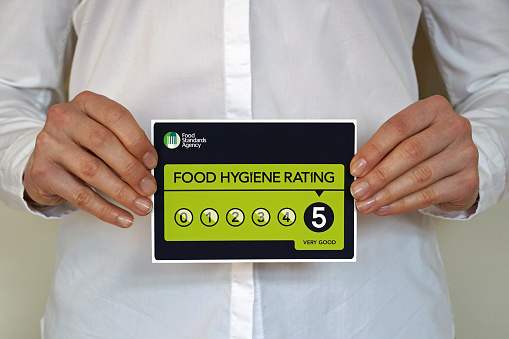 Restaurant manager holds a sticker with Food Hygiene rating 5 from The United Kingdom Food Standards Agency