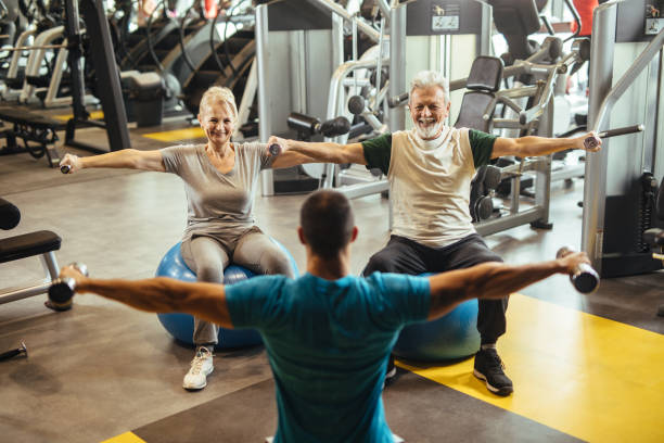 istock Senior couple exercising with personal trainer using dumbbells at the gym 1219130680