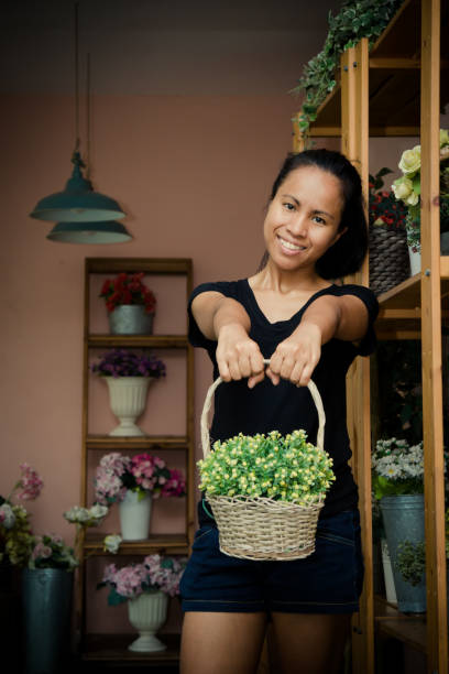 アジアの女性オーナーが黄色と緑の花を持つバスケットを店内に持っている - florist supermarket flower bouquet ストックフォトと画像