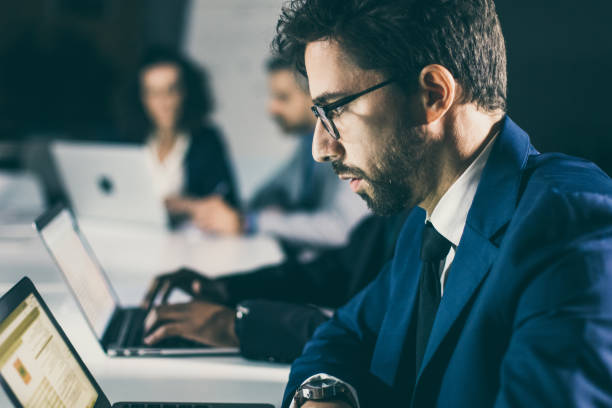 istock Serious businessman sitting at table and looking at laptop 1219137671