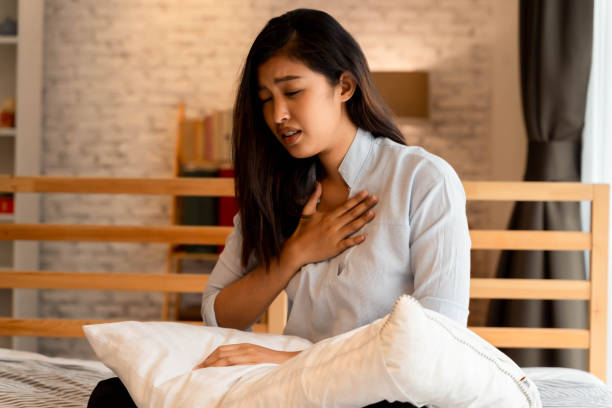 Portrait of 20s young Asian woman having difficulty breathing in bedroom at night. Shortness of breath, asthma, difficult to breathe problems stock photo