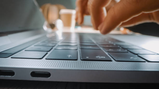 istock Close-up Moving Macro Shot: Person Typing on Laptop Keyboard. Working, Writing Emails, Using Internet. Notebook lying on the Table, Bright Sunny day in Background 1219143129
