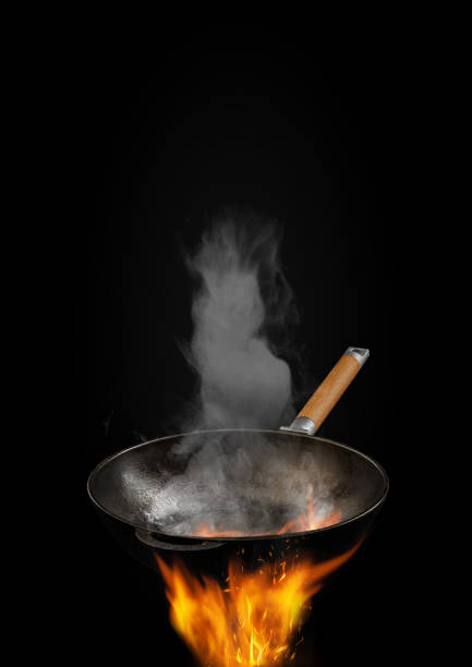 istock Empty burning wok pan with smoke above fire against black background. Cooking concept. Mockup, template for your collage, text or images. Close up 1219144064