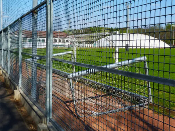 Abandoned, empty soccer and sport field behind galvanized metal fence. goal turned on the side symbolizing out of use and service. lock down of sport facility due to Covid-19 and Coronavirus. bright green turf grass