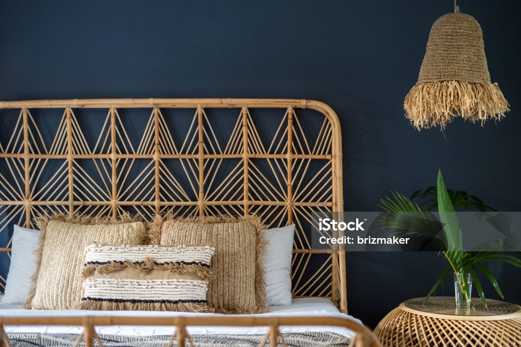 Traditional asian interior bedroom at cozy house with ethnic decor Traditional asian interior bedroom at cozy house with ethnic decor, wicker headrest at comfortable bamboo bed, lamp over nightstand table and natural green plant composition Furniture Stock Photo
