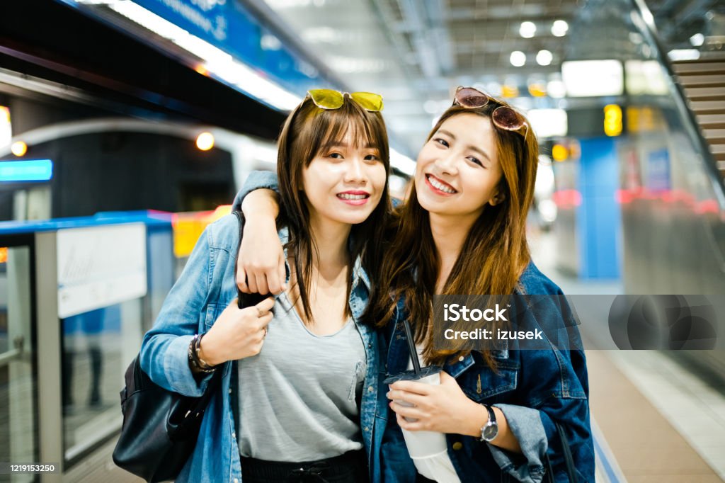Female friends at subawy station Two young women are standing at subway station, embracing and smiling at camera. They are spending weekend together. Taiwan Stock Photo
