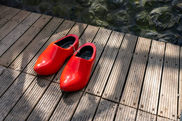 Pair of red wooden shoes hanging on an old dark wooden wall. Traditional alpine decoration symbolizing Swiss heritage and craftsmanship.