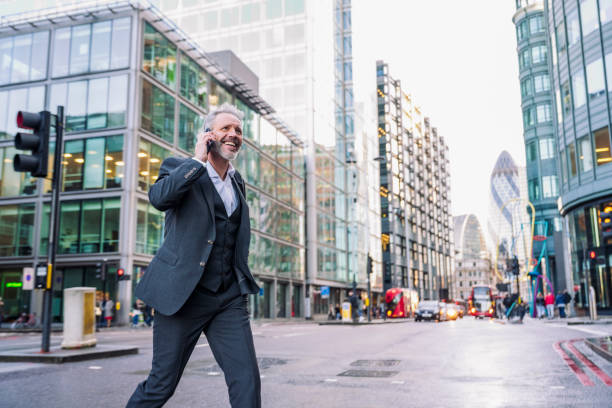 Smiling London businessman using phone while crossing street