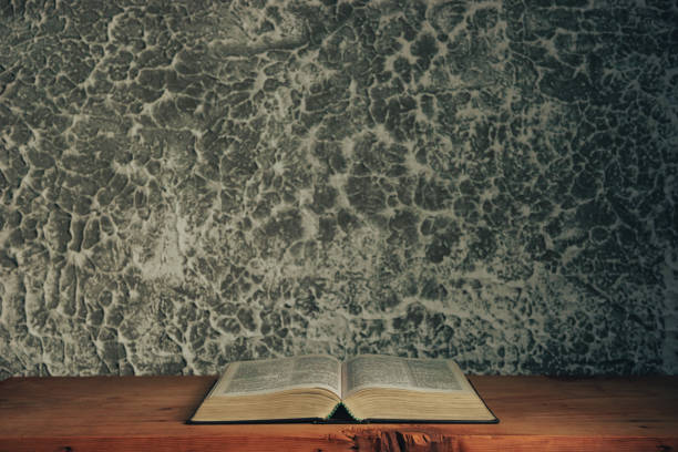 istock Open bible on a brown old wooden table. Beautiful gray white wall background. 1219154898