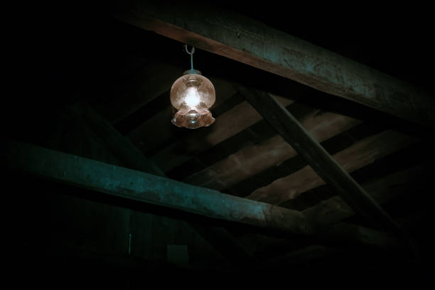 in Mystical horror scary garret background to halloween. Old antique dirty wooden ceiling with beams and a lamp in the darkness in a mysterious paranormal frightening basement or attic with black shadow interior of old house garret stock pictures, royalty-free photos & images