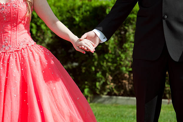 Girl dressed in red for prom holding hands with date stock photo