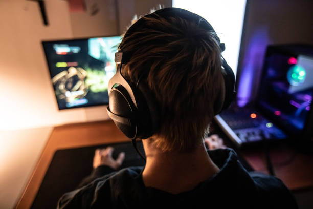 rear view of gamer with headset on playing online video games in dark room - stock photo - escape from it all fotos imagens e fotografias de stock