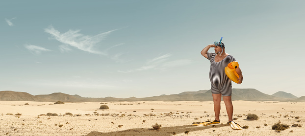 Funny overweight swimmer looking for the beach  in the middle of the desert with copy space