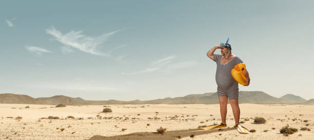 Funny overweight swimmer searching for the beach in the middle of the desert Funny overweight swimmer looking for the beach in the middle of the desert with copy space tourist lost humor confusion stock pictures, royalty-free photos & images