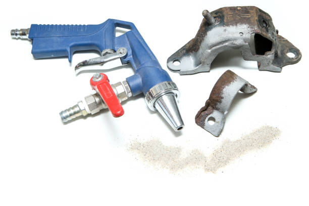 The overgrown rusty cast iron part partly sand blasted together with sand and blasting gun isolated in a white background.