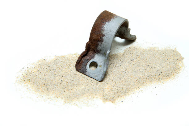The overgrown rusty cast iron part partly sand blasted together with sand isolated in a white background.