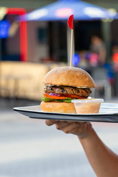 istock Female hand holding a beef hamburger with lettuce and tomato and grilled bread on a table, outdoors 1219166177