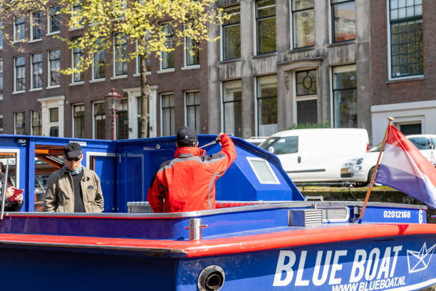 Canal during a bright spring day in Amsterdam, Netherlands with a tour boat/water bus on the canal passing the photographer on another water bus.