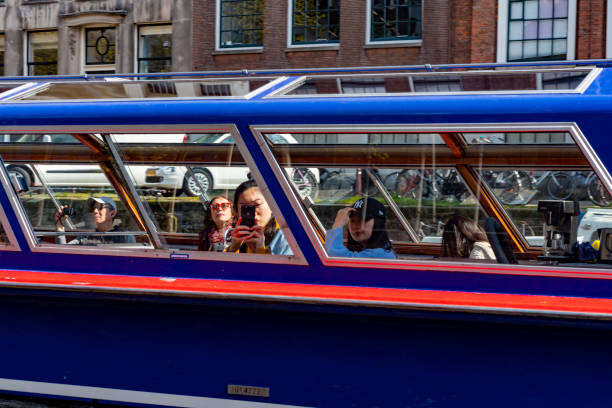 Canal during a bright spring day in Amsterdam, Netherlands with a tour boat/water bus on the canal passing the photographer on another water bus.