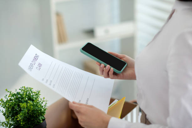 istock Female hands holding unemployment claim and mobile 1219167854