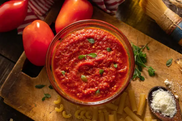 Italian tomato sauce "Napoli" style surrounded by  some tomatoes, parmesan cheese, fresh oregano leaves and uncooked pasta. "Napoli" (Naples) is a very simple traditional Italian sauce, made with few ingredients (tomato, garlic, onion, oregano, salt and olive oil). 
This sauce can also be used with other kind of food such as pizza, meats or vegetables, on a bruschetta or as a dip. Due its simplicity, it is a very versatile sauce.