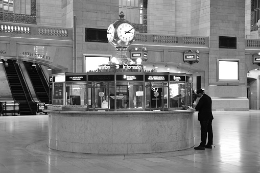 The central information booth with it's clock is an iconic spot of New York's Grand Central Terminal.  During the pandemic the terminal is nearly empty, yet there are still a few people who are hanging around either waiting for a train for just distancing themselves.
