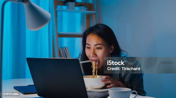Asia Freelance Smart Business Women Eating Instant Noodles While Working On Laptop In Living Room At Home At Night Stock Photo - Download Image Now