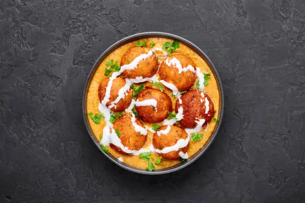 Malai Kofta Curry in black bowl at dark slate background. Malai Kofta is indian cuisine dish with potato and paneer cheese deep fried balls in onion tomato gravy with spices. Indian Food.