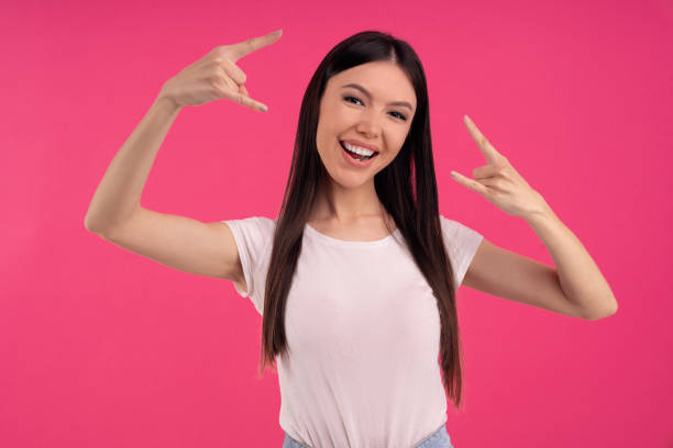 istock Pleasant looking cheerful woman make rock sign, gestures with both hands, feels rebellious, shows heavy metal, goes wild, listens loud music at home, dressed casually. Asian girl has fun at party 1219177103