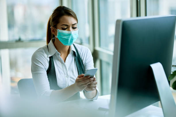 istock Businesswoman wearing face mask while using mobile phone in the office. 1219180515