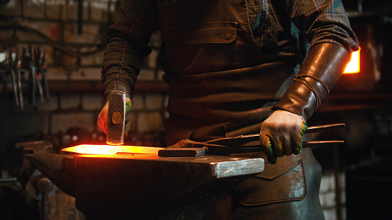 Blacksmith working in the workshop - man hitting the hot red metal with a hammer. Mid shot