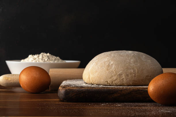 istock Fresh raw dough for bread or pizza with eggs on a dark wooden table. 1219186324